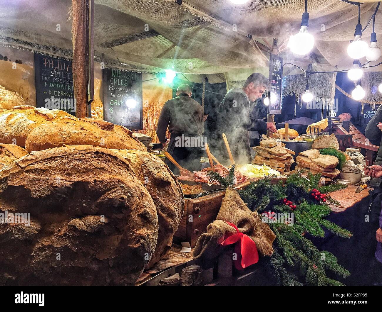Un chiosco di cibo al mercato di Natale di Cracovia vende pane e cibi caldi, creando un'atmosfera di vacanza calda e accogliente con prelibatezze tradizionali polacche - Immagine stock catturata con smartphone