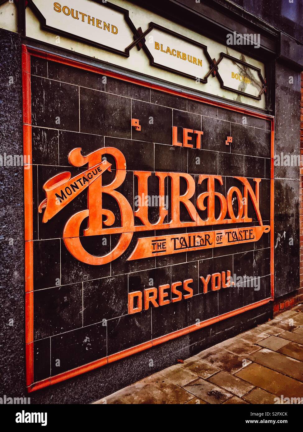 Lasciate che Montague Burton vestiamo... Il sarto di gusto. L'originale degli anni Trenta in stile Art Deco rilievo rivestito di piastrelle al di fuori del Menswear Burtons Shop ad Abergavenny, Wales, Regno Unito. - Immagine stock catturata con smartphone
