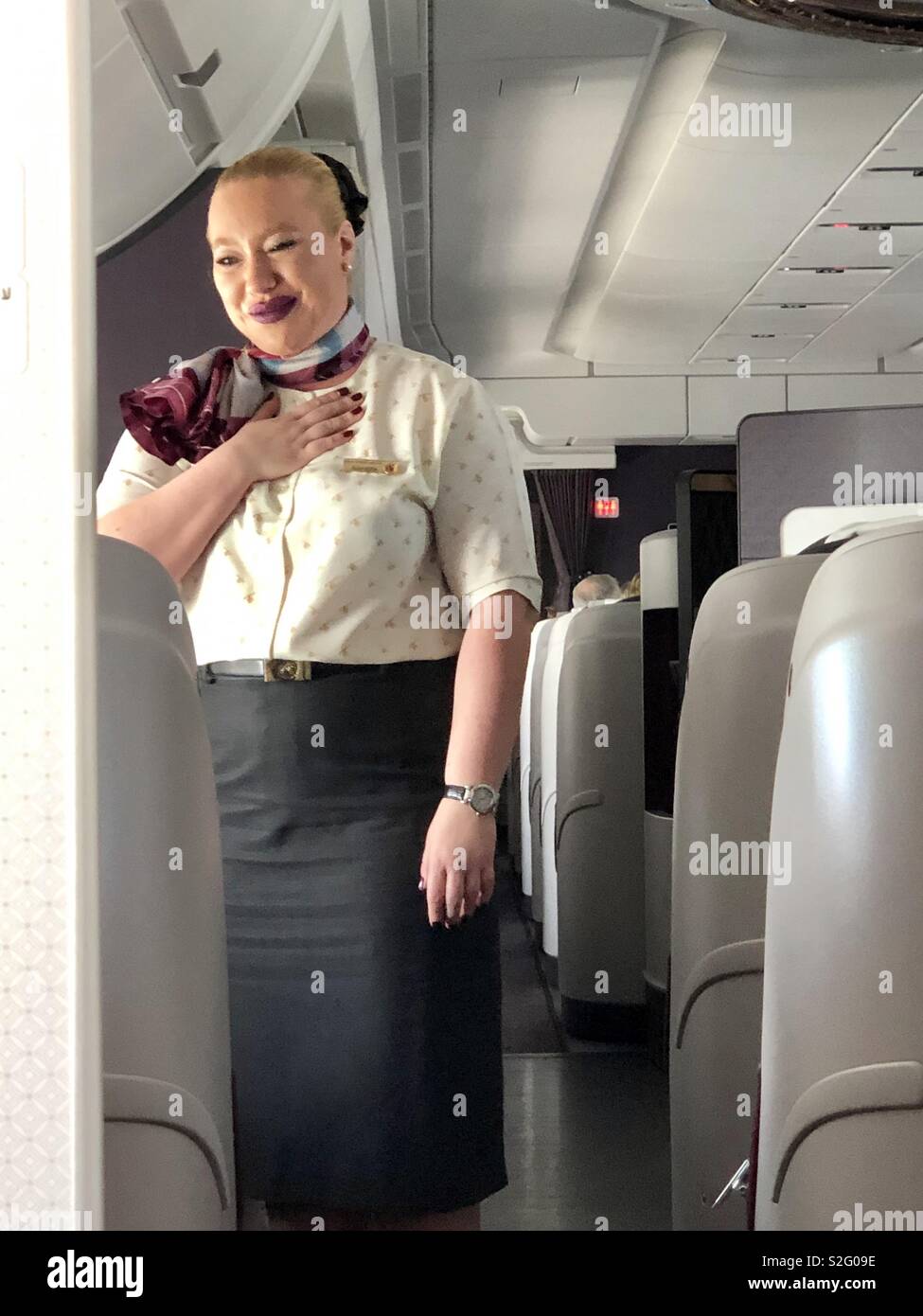 Un senior assistente di volo dire grazie con la sua mano sul suo cuore con gratitudine ai passeggeri in business class di un Airbus A350 della Qatar Airways. Foto Stock