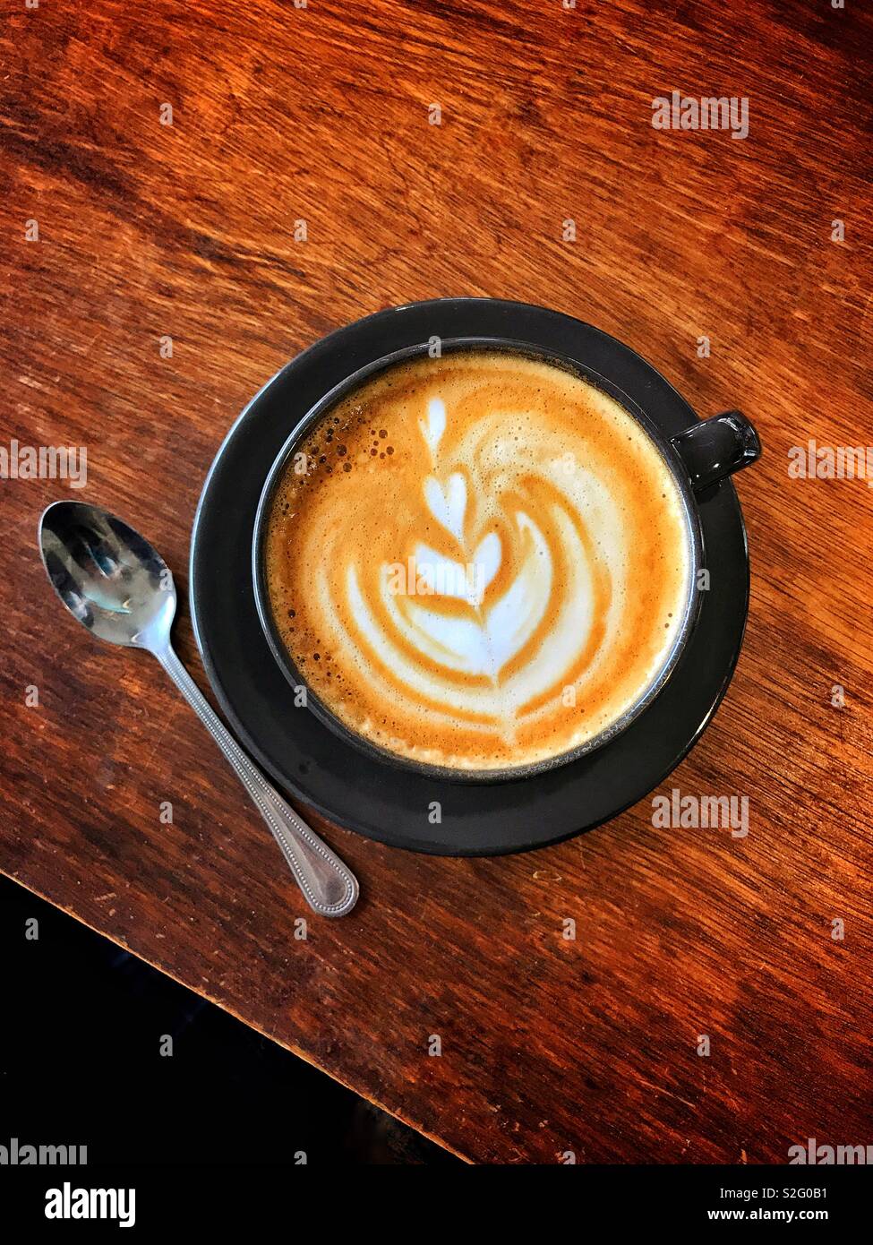 Un overhead immagine di una tazza di caffè latte macchiato. Cucchiaio è sul tavolo di legno. Non vi è lo spazio per la copia o il testo o nella parte superiore o inferiore dell'area della foto. Foto Stock