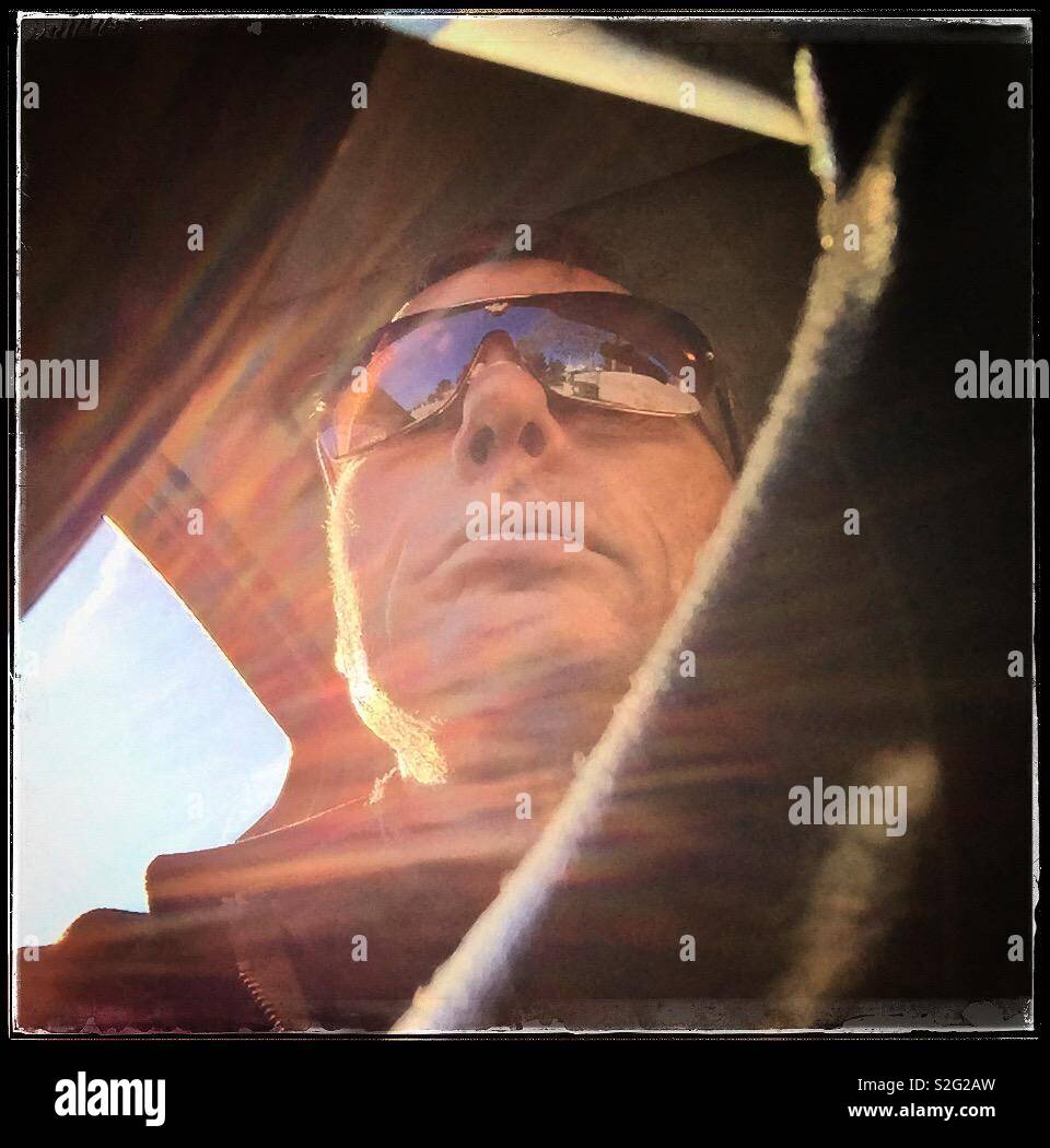 L uomo nel sedile di guida di una vettura con Sun sulla finestra e un cielo limpido, Spagna. Foto Stock