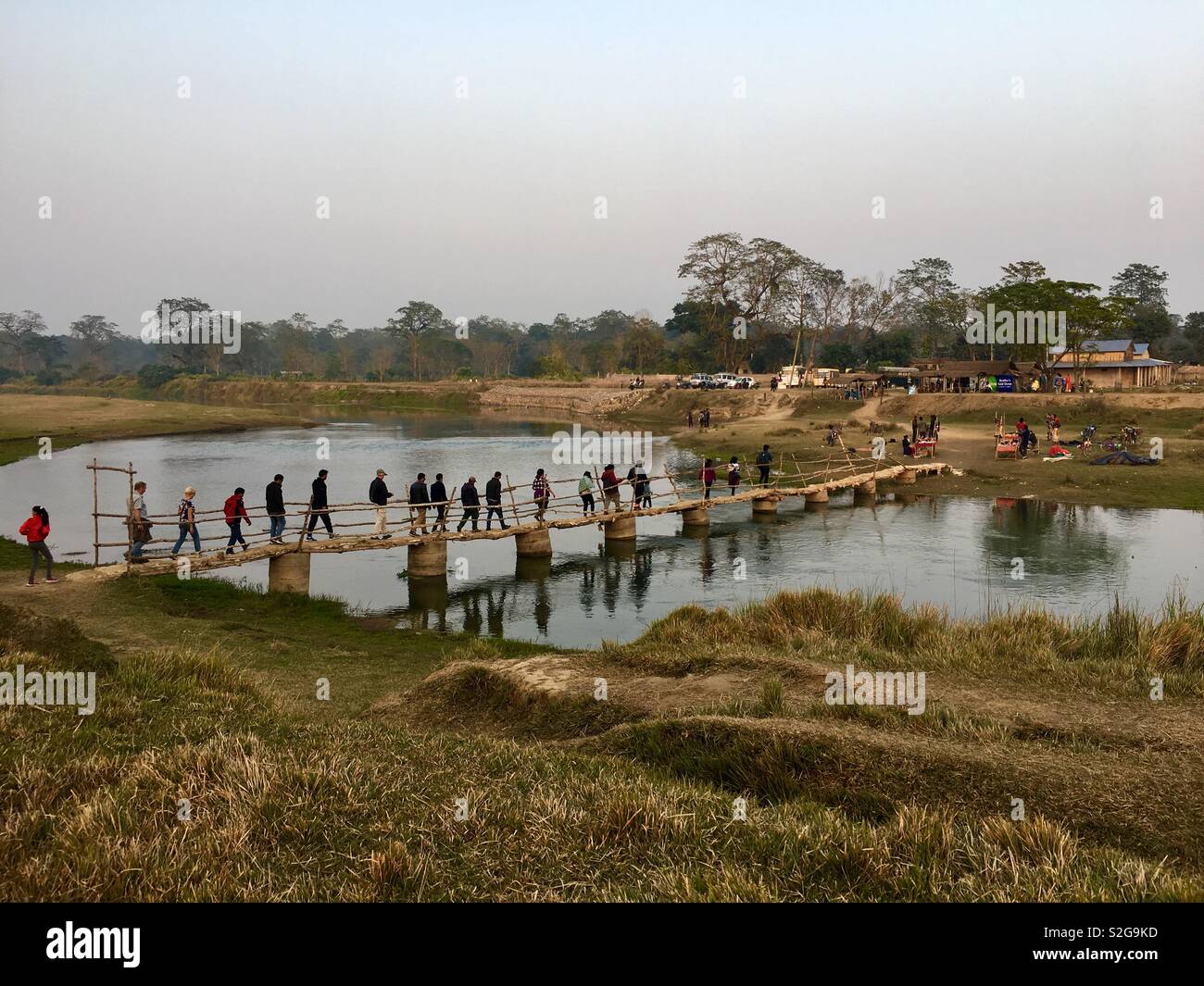 Visitatori attraversando ponte pedonale di fronte fiume Narayani all'elefante allevamento e centro di formazione di Chitwan il parco nazionale, il Nepal. Foto Stock
