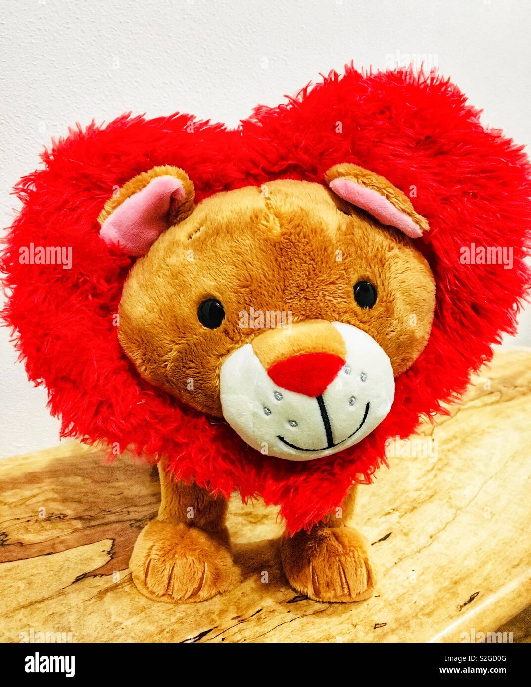 Carino sorridente Lion animale farcito con criniera rosso a forma di cuore sul legno pietrificato panchina - Immagine stock catturata con smartphone