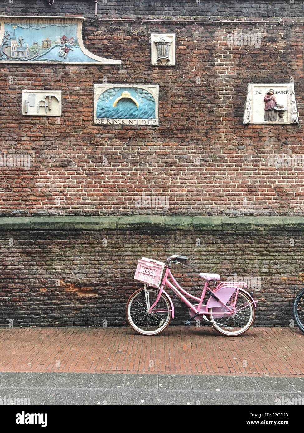 Bicicletta rosa di fronte a un muro di mattoni decorata con placche in Amsterdam Foto Stock