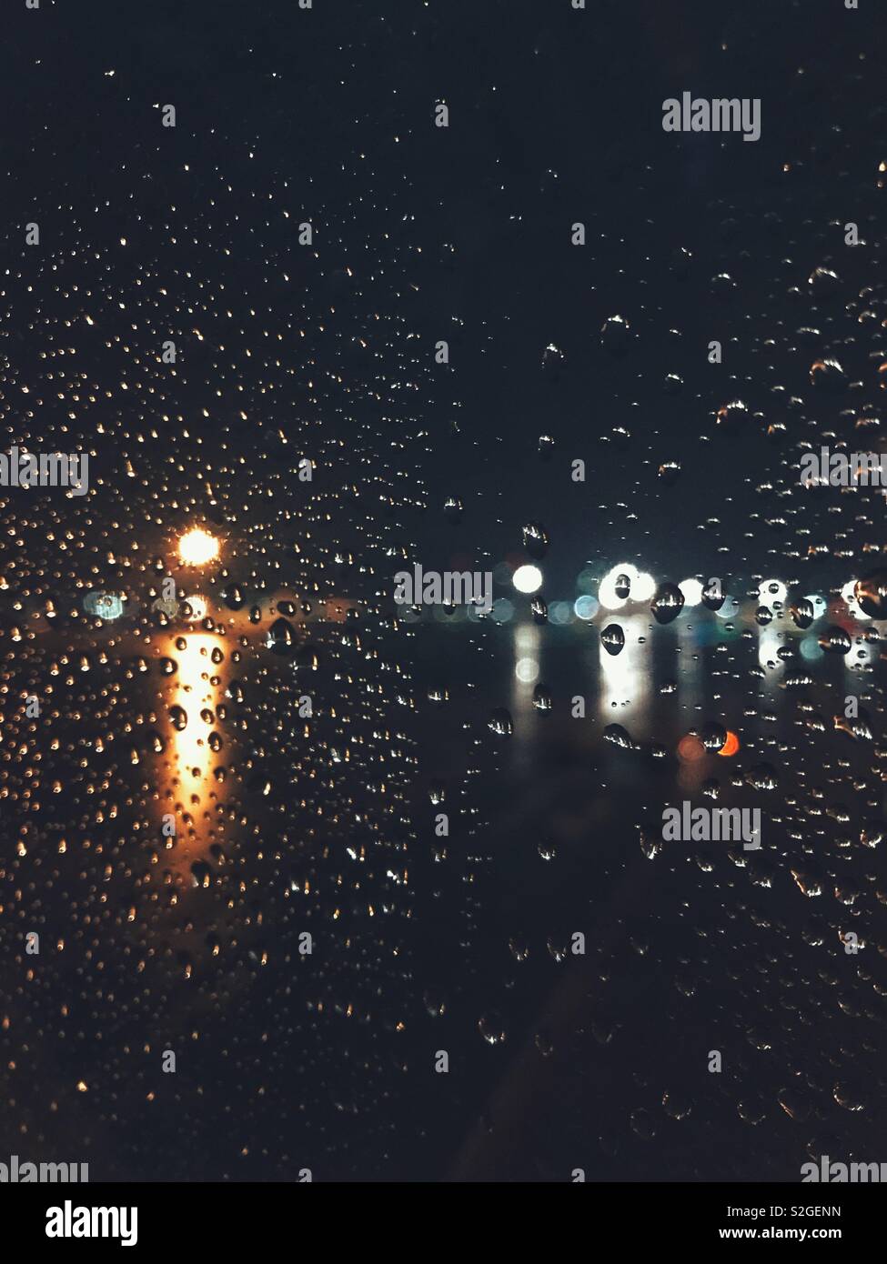 Gocce di pioggia su una finestra con sfondo sfocato luci di notte Foto Stock