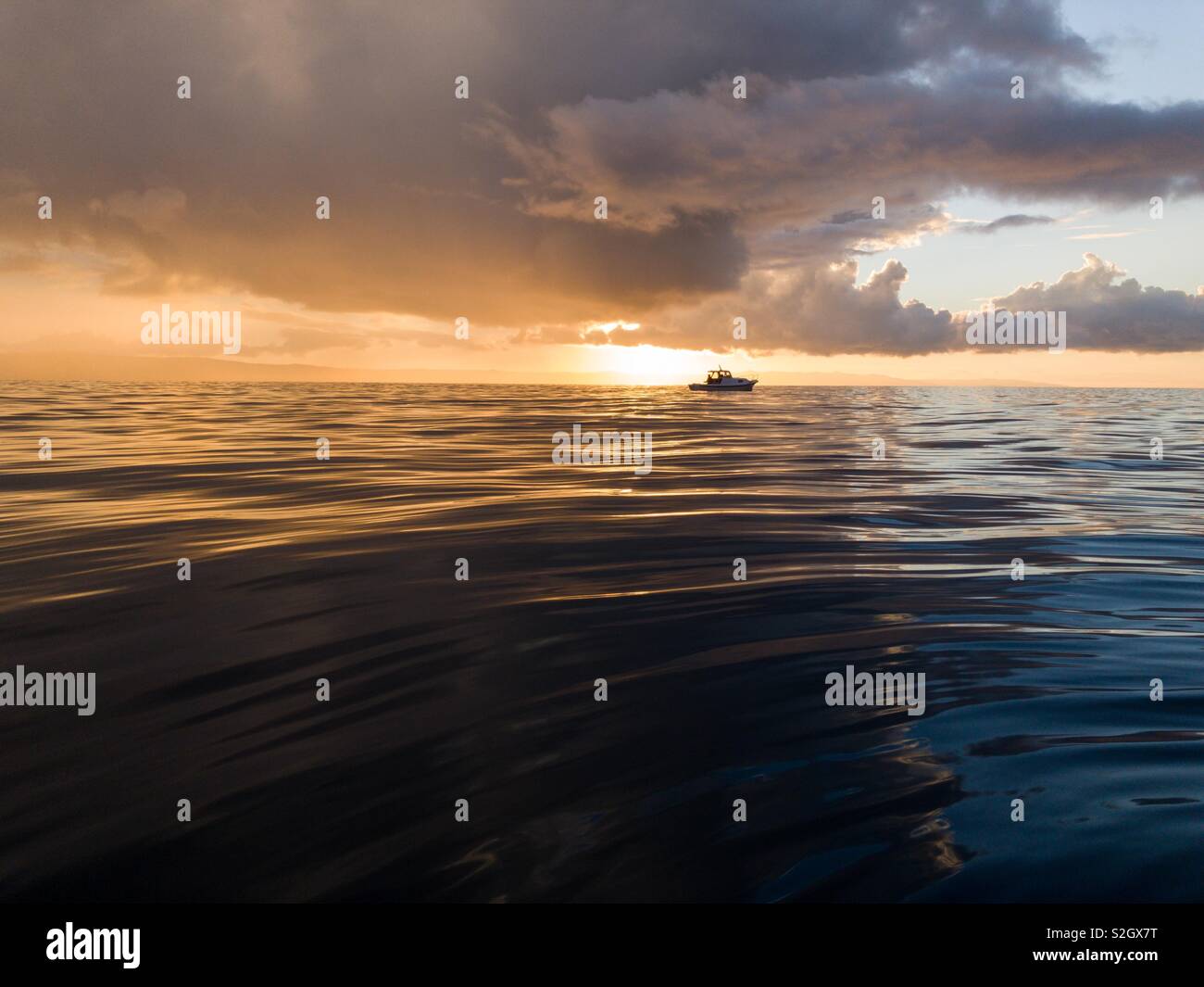 Piccola barca sul mare calmo al tramonto colorato Foto Stock