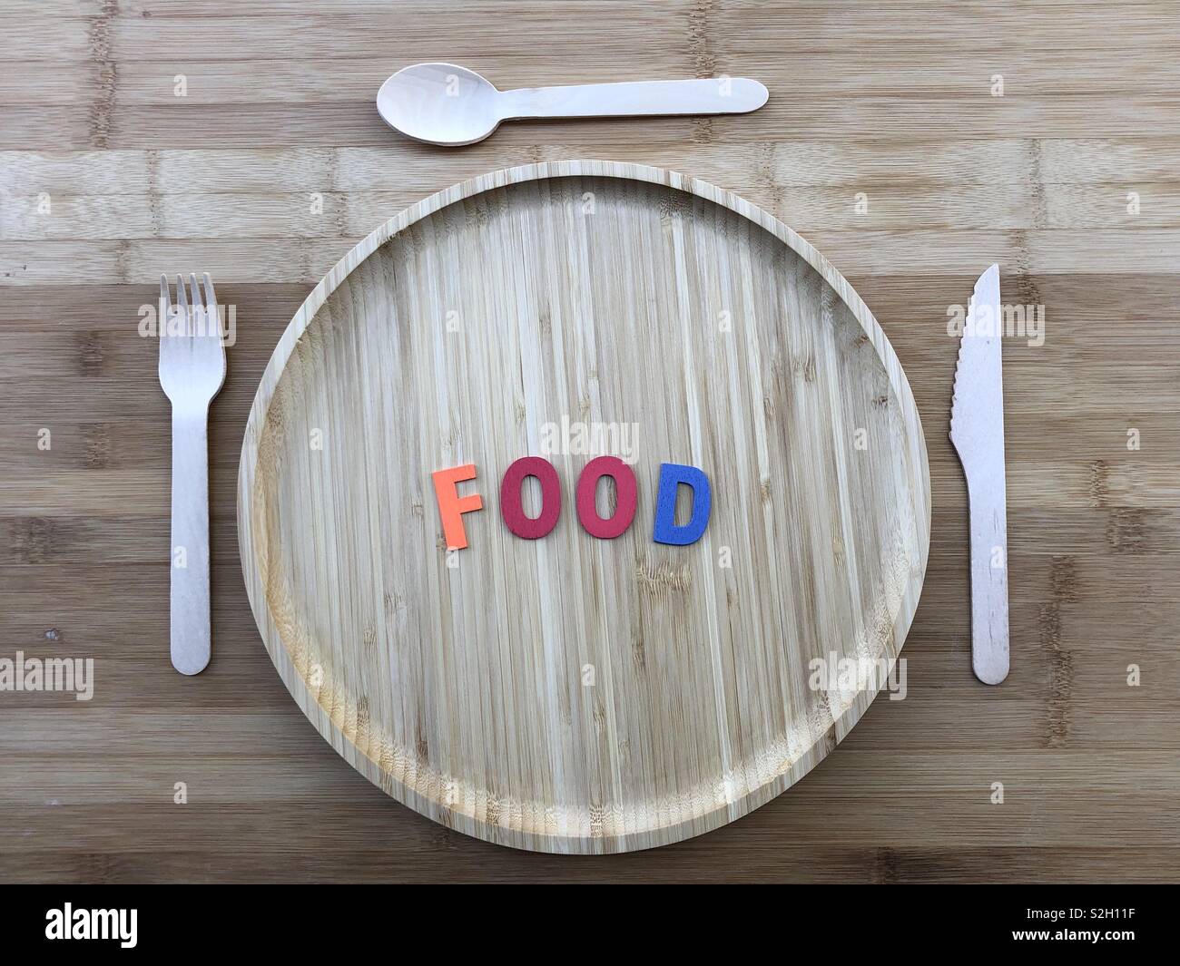 Piatto di legno con posate di legno su una tavola di legno abd di legno colorato lettere della parola cibo - Immagine stock catturata con smartphone