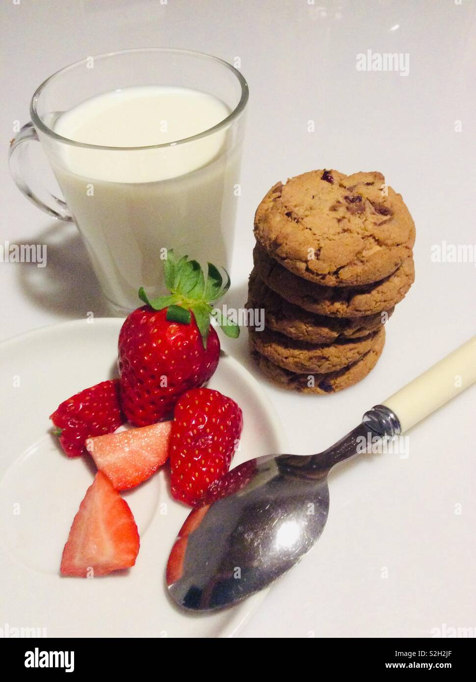 La prima colazione con un bicchiere di latte fresco Fragole, mirtillo palustre e biscotti al cioccolato Foto Stock