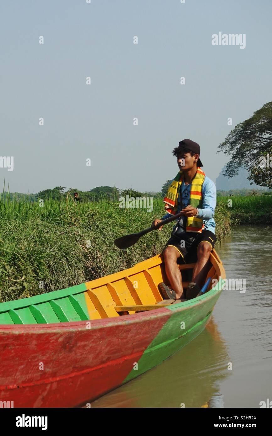 Uomo birmano su un tradizionale canotto in legno. Accanto a un campo di riso in Myanmar Birmania. Foto Stock