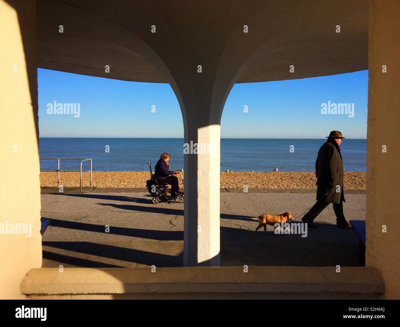 Una donna su uno scooter di mobilità e un uomo a camminare lungo la passeggiata dalla spiaggia a trattare, Kent, Regno Unito - Immagine stock catturata con smartphone