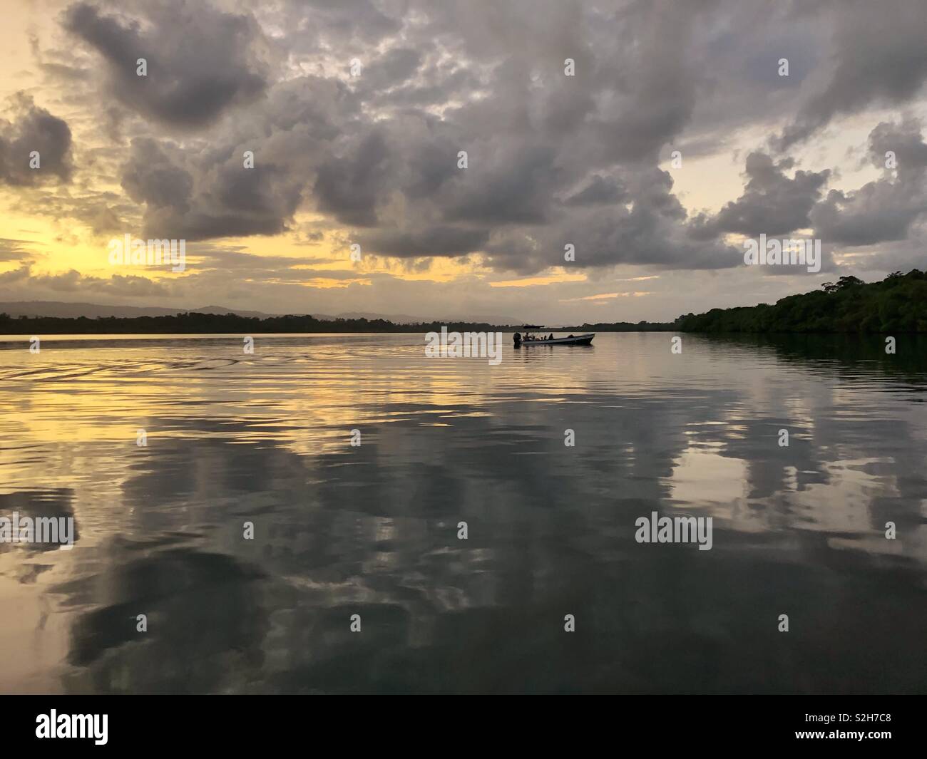 Piccola barca si avvicina Cristobal Island al tramonto, con Tierra oscura in background - Bocas del Toro, Panama Foto Stock