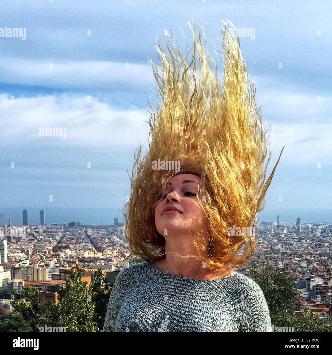 Ritratto di una ragazza bionda con lunghi capelli ricci che il vento è sventolata. Essa sorge su una collina al di sotto della città e il mare è visibile. Foto Stock