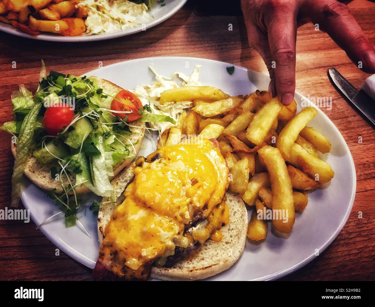 Una mano ruba un chip da una piastra con un formaggio gourmet burger e insalata mista Foto Stock