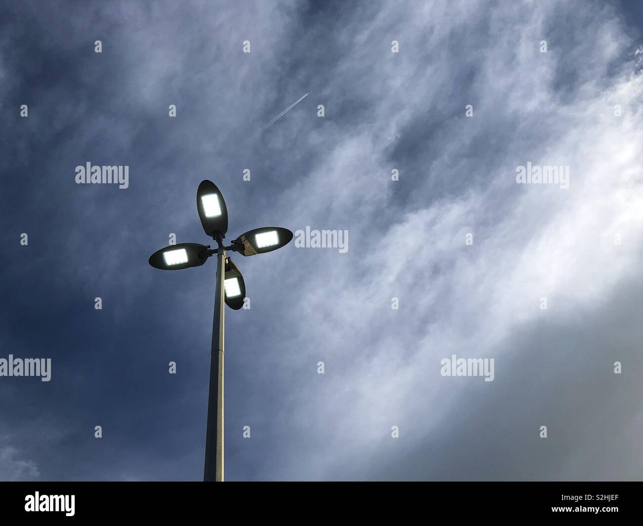 Lampione contro il cielo tempestoso e aereo chem sentieri. Foto Stock