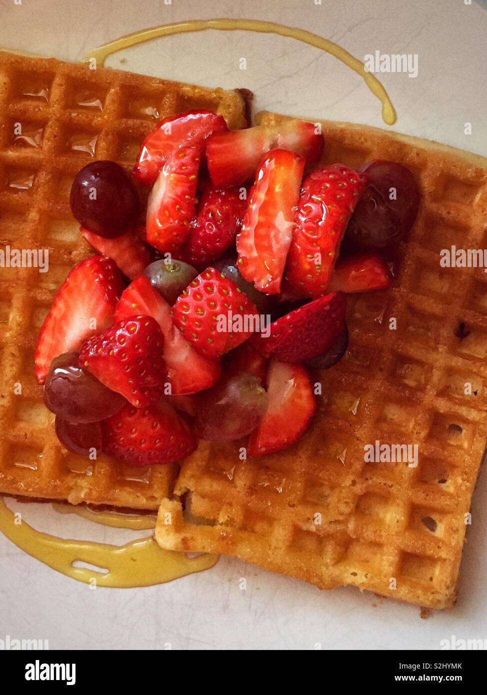 Cialde con frutta e sciroppo per la prima colazione. Dolce e gustose fragole e uva con sciroppo dorato sopra la parte superiore delle cialde burroso. Foto Stock