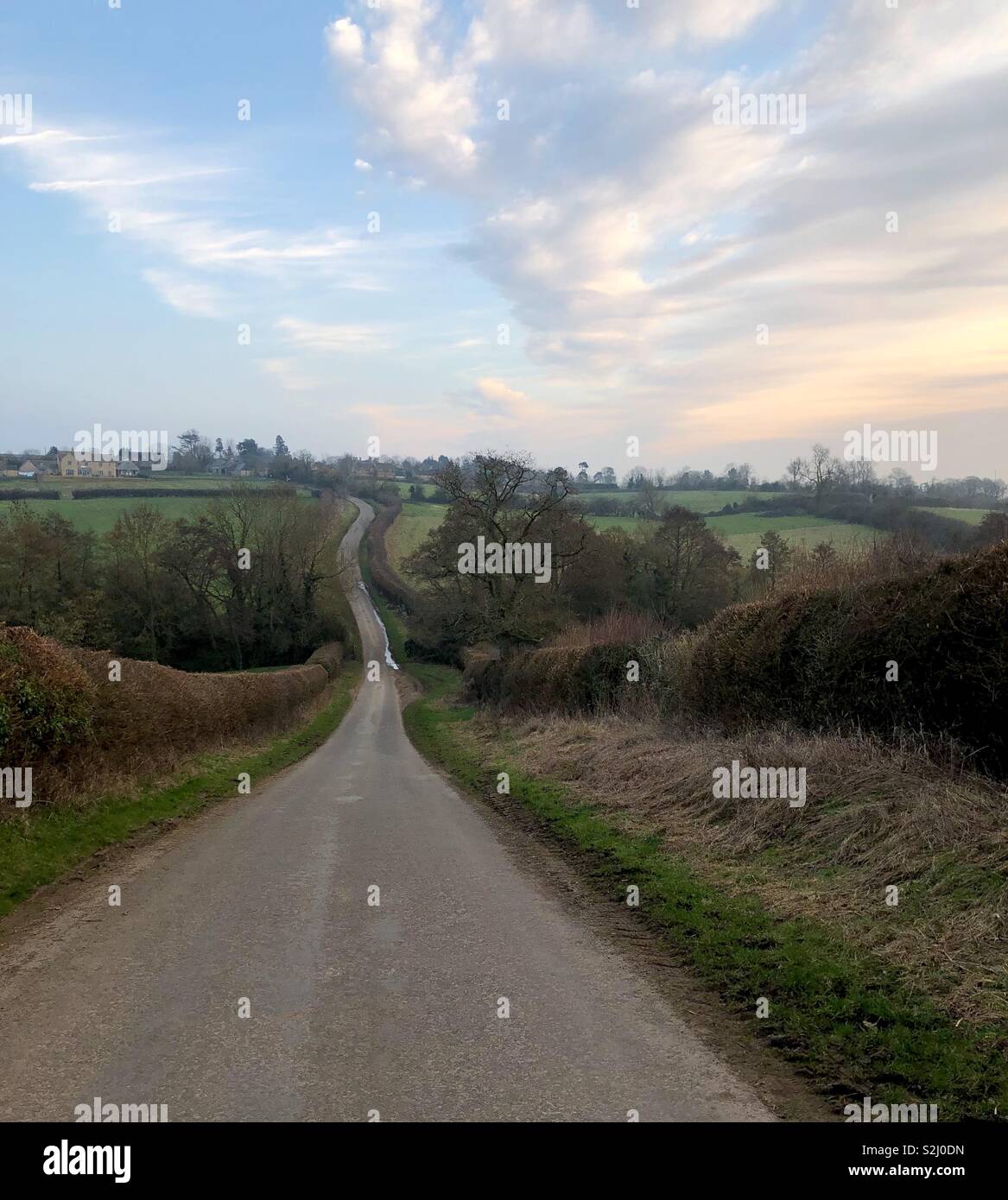 Un maturo di scena di strada di un paese misteriosamente avvolgimento verso l'orizzonte e un villaggio Costwold sulla cima di una collina. - Immagine stock catturata con smartphone
