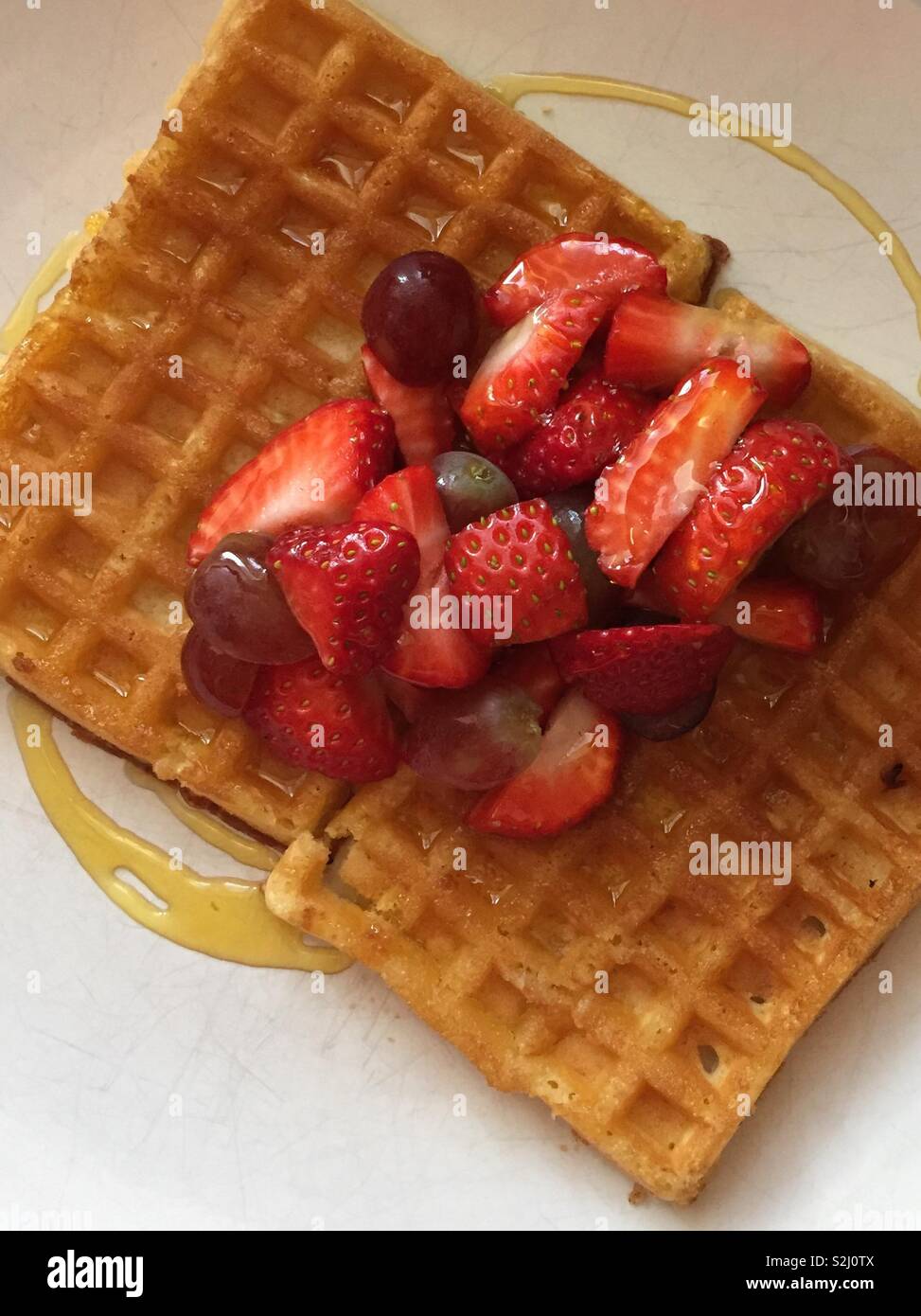 Fresca frutta vibranti che comprende le fragole su hot waffles belgi. Colazione perfetta, dessert o cibo di strada trattare - Immagine stock catturata con smartphone