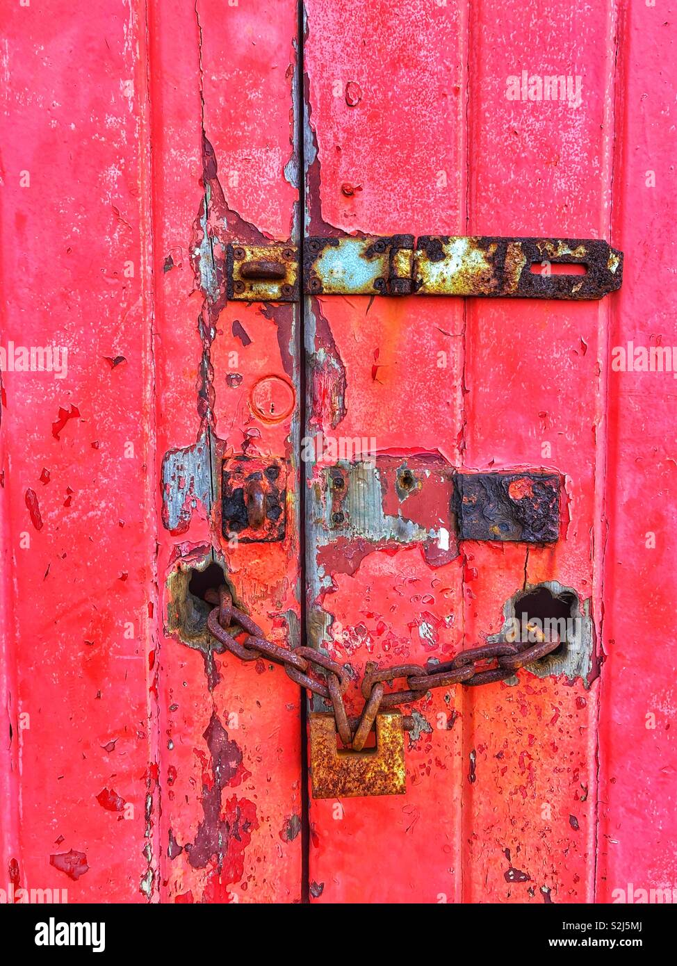 Il vecchio si blocca su una vecchia porta di garage con peeling vernice rossa. Foto Stock