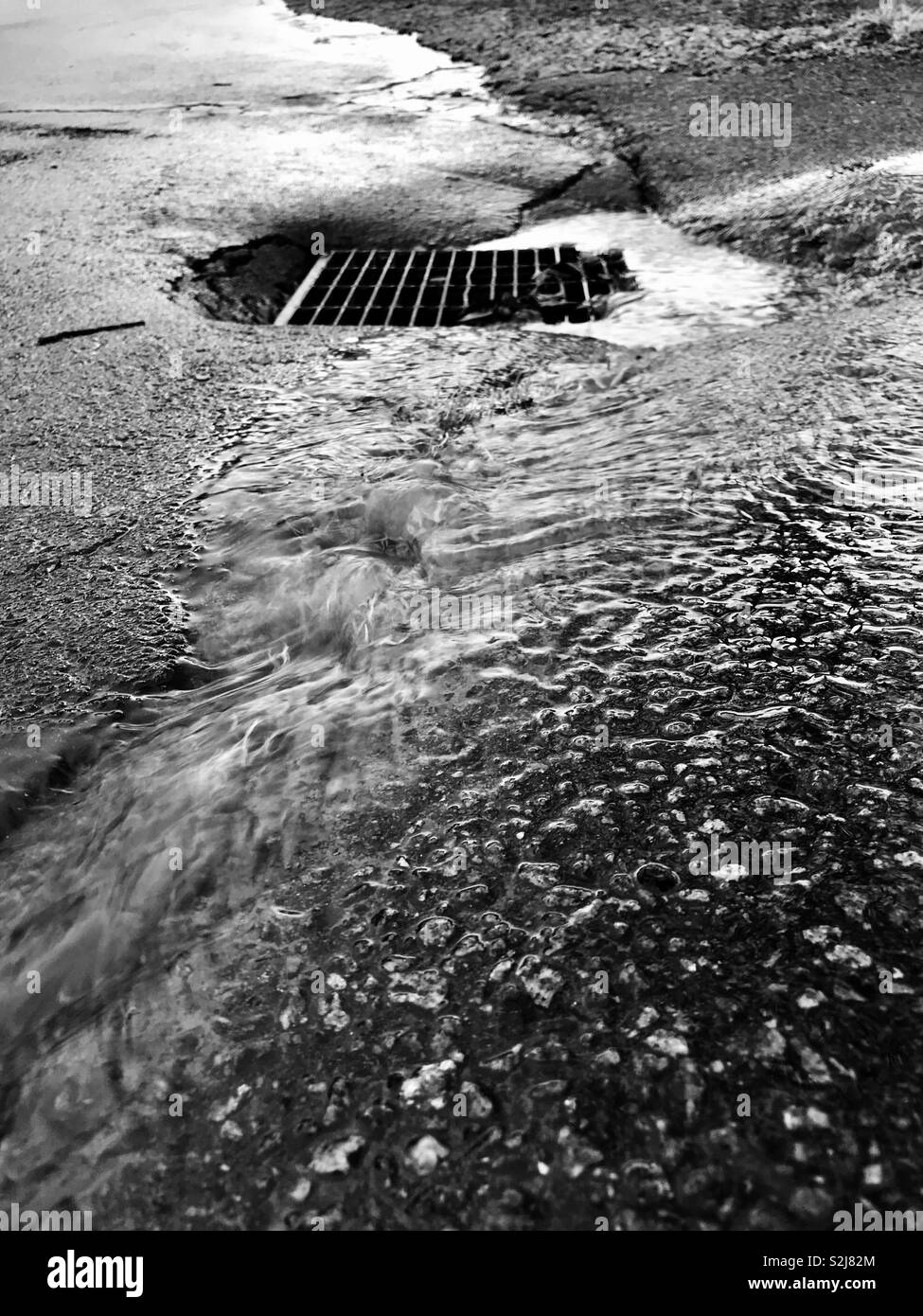 L'acqua piovana fluisce nella tempesta scaricare su pavimentazione ruvida- in bianco e nero Foto Stock