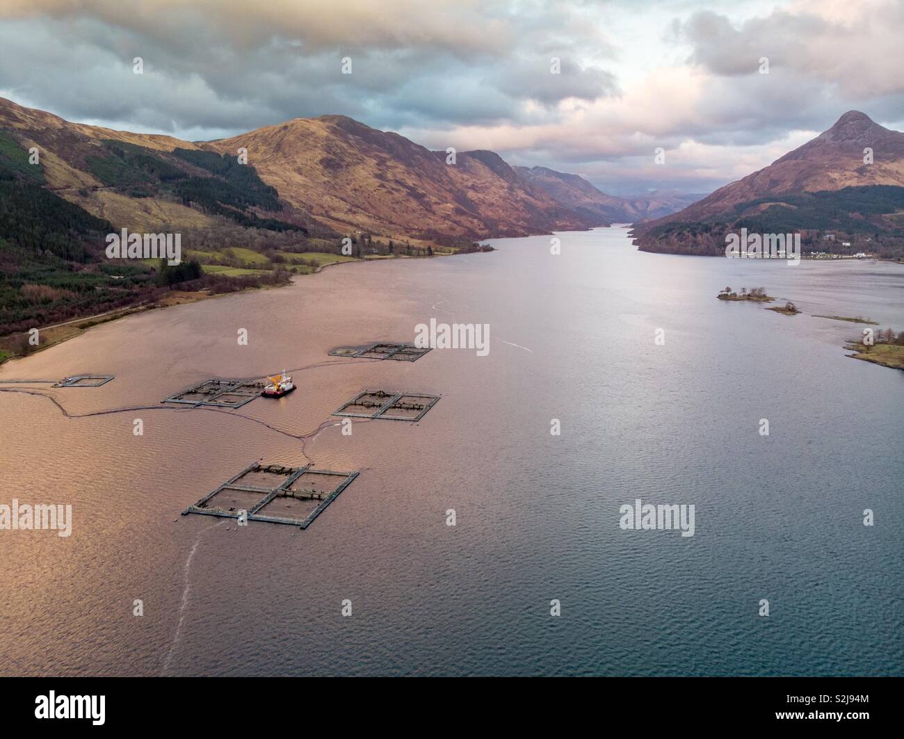 L'allevamento di salmoni sul Loch Leven in Scozia con il Pap di Glencoe a destra. Foto Stock