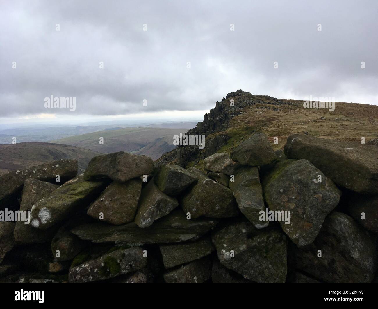 Vertice di montagna e un muro di pietra sotto tempestoso cielo grigio - Immagine stock catturata con smartphone