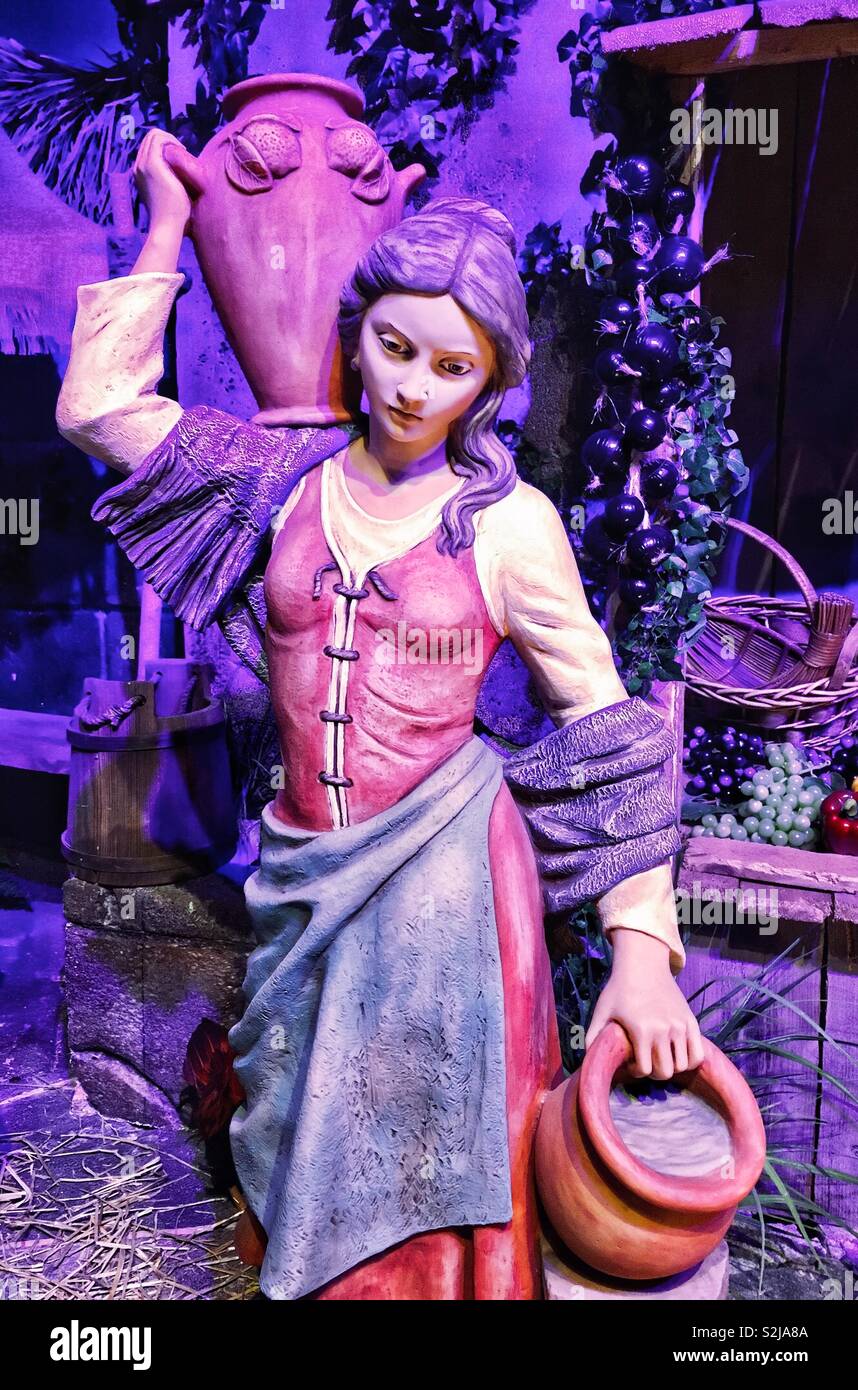 Emanuele Fontanini cimelio di famiglia natività statua di capelli lunghi donna in abito rosso con viola scialle e grembiule blu che trasportano acqua in caraffe da frutta stand nella città di Betlemme - Immagine stock catturata con smartphone