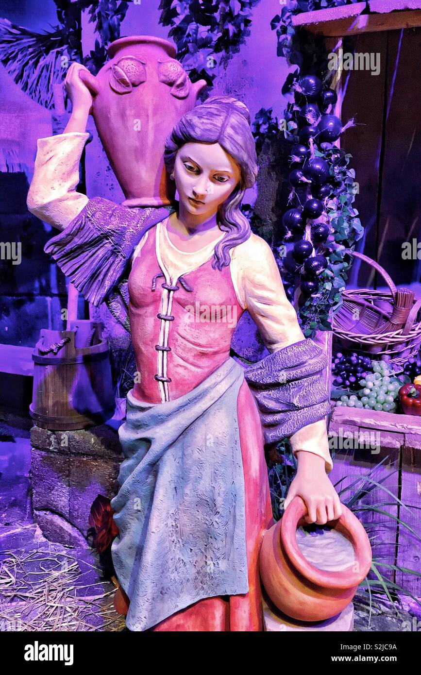 Emanuele Fontanini cimelio di famiglia natività statua di capelli lunghi donna in abito rosso con viola scialle e grembiule blu che trasportano acqua in caraffe da frutta stand nella città di Betlemme - Immagine stock catturata con smartphone