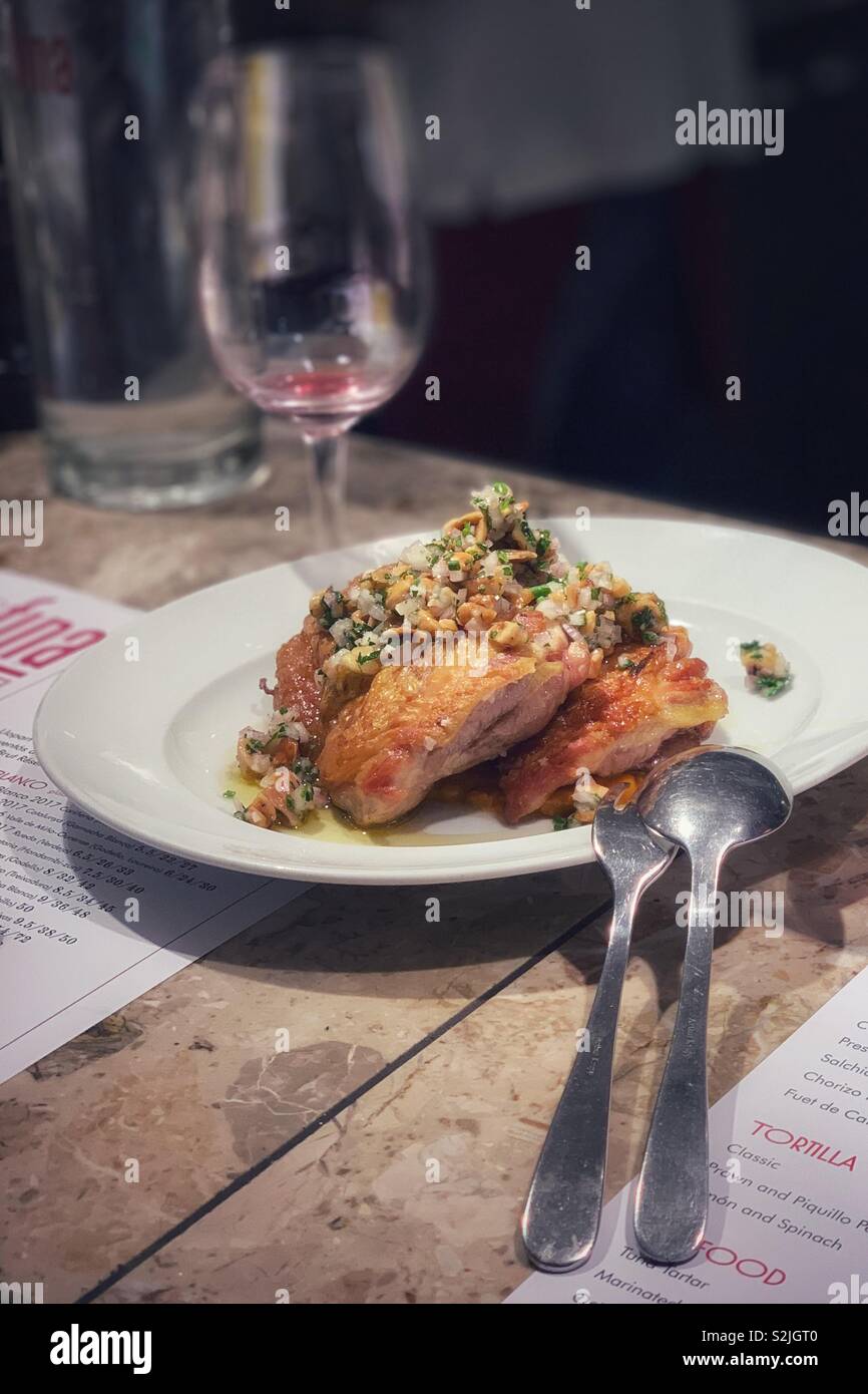 Pollo condito con anacardi su una piastra bianca lungo con un bicchiere vuoto di vino e di argenteria in un ristorante Foto Stock