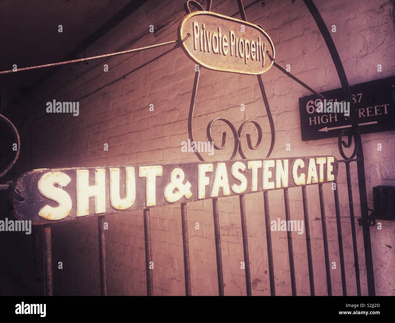 Entrata con cancello vintage che mostra i cartelli "Private Property" e "Shut & Fasten Gate" al 69-87 di High Street, che richiamano un'atmosfera urbana classica - Immagine stock catturata con smartphone