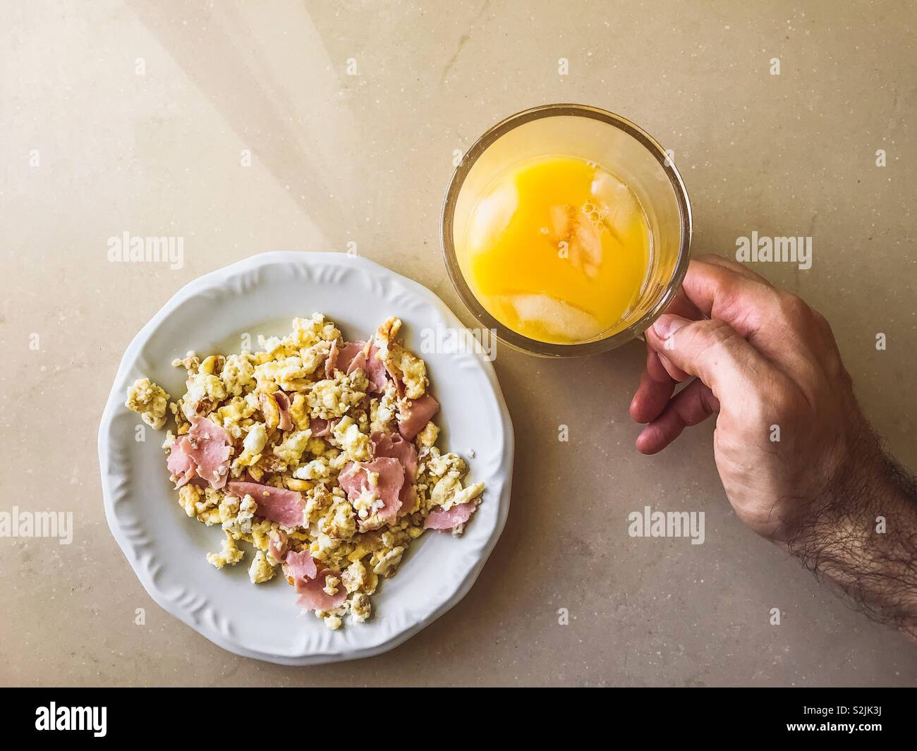 Punto di vista personale di un uomo di fare colazione con uova strapazzate e succo di arancia Foto Stock