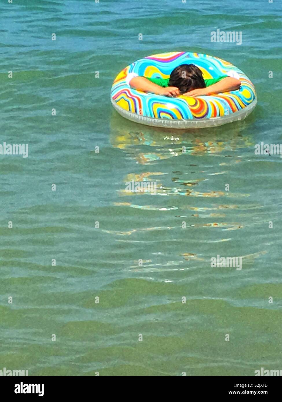 Giovane uomo nuotare nel mezzo del lago, con un tubo interno rilassante durante un estate spiaggia gita. Foto Stock