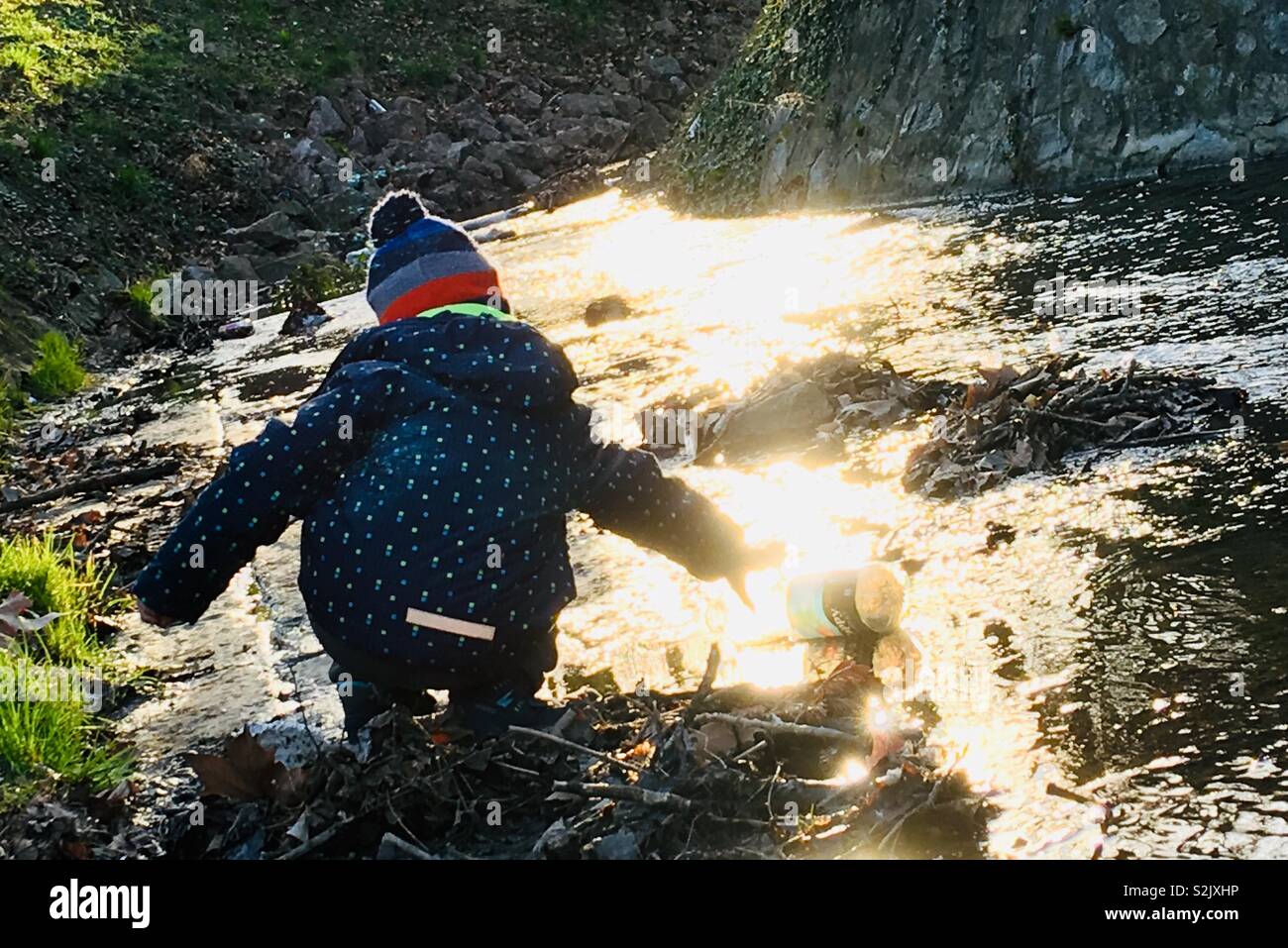 Bambino raggiungere fuori per immondizia la bottiglia di plastica nel ruscello - Immagine stock catturata con smartphone