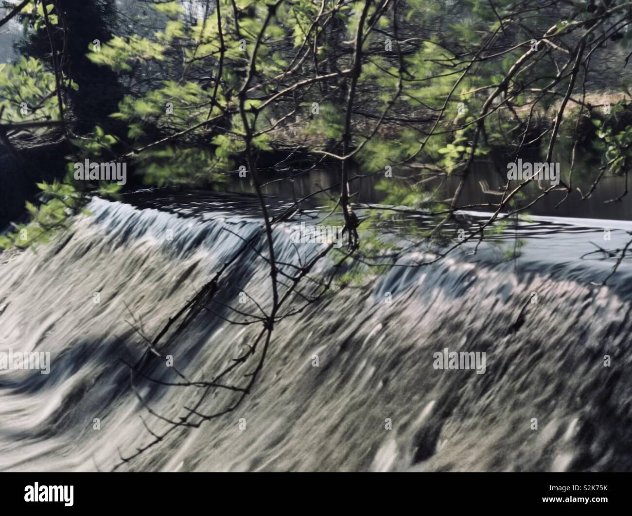 Cascata di acqua su un piccolo weir in bright sole primaverile, una lunga esposizione acquisiti su iPhone x Foto Stock