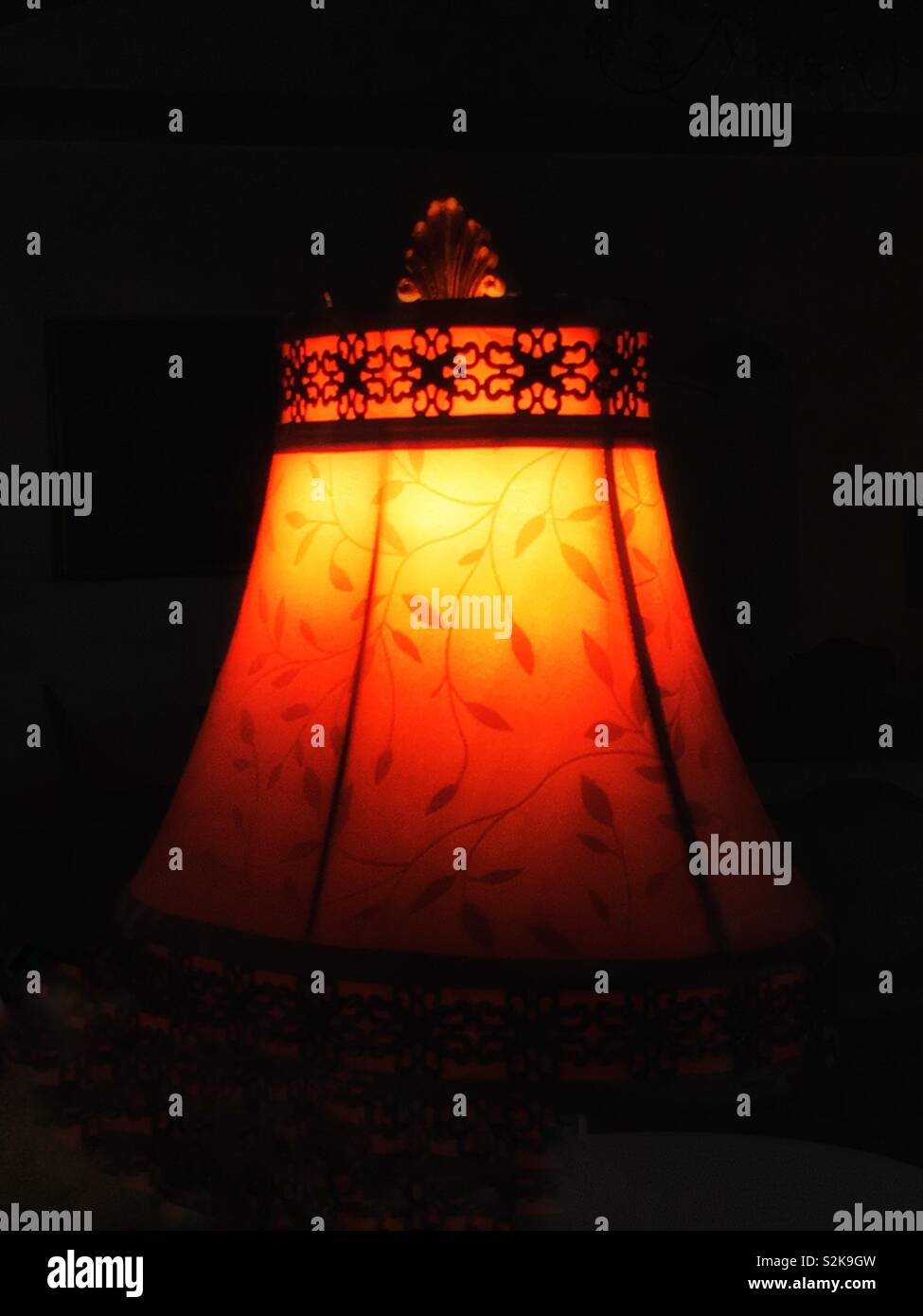 Luce calda da una lampada accesa e paralume in una stanza buia. Foto Stock