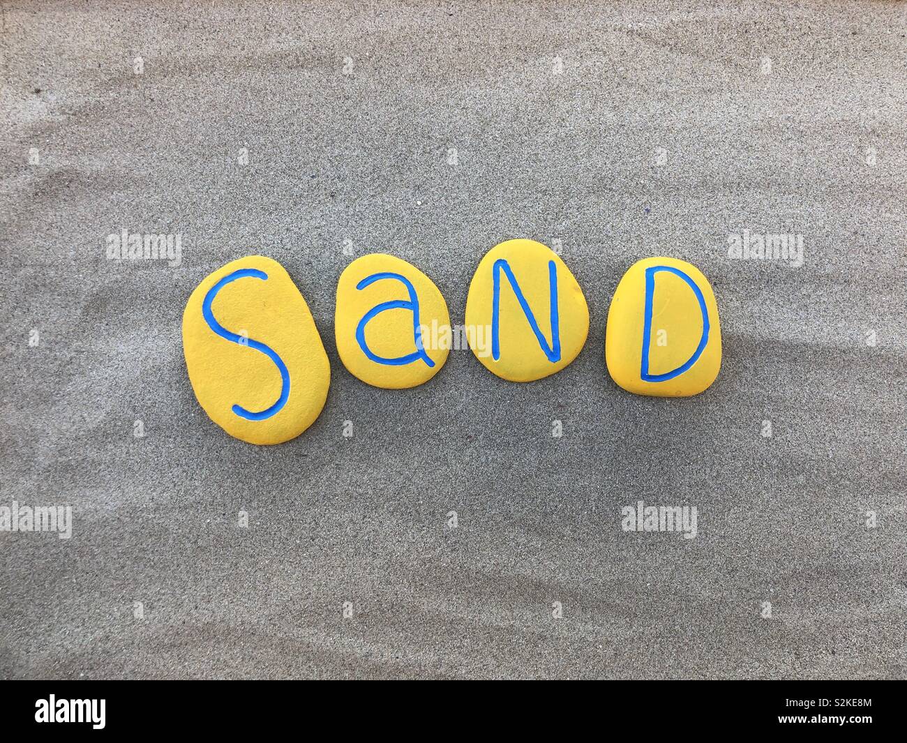 Sabbia parola composta con verniciato giallo pietre sulla spiaggia - Immagine stock catturata con smartphone