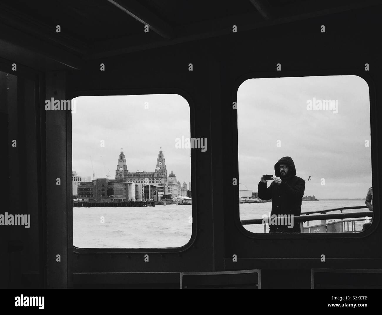 Vista degli edifici di fegato attraverso Mersey ferry finestra con uomo prendendo una foto in altra finestra. Lo skyline di Liverpool Foto Stock