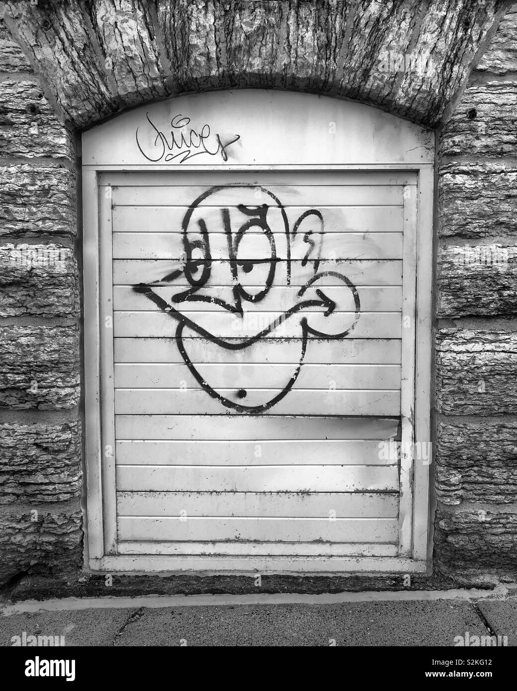 Graffiti su una piccola porta metallica circondata da pietra storica. Foto Stock