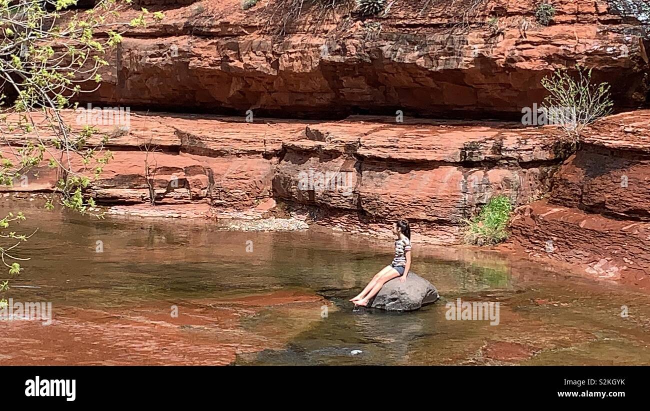 Un tween ragazza si siede su una roccia in un torrente nel Canyon di Oak Creek portano a Sedona, in Arizona. Foto Stock