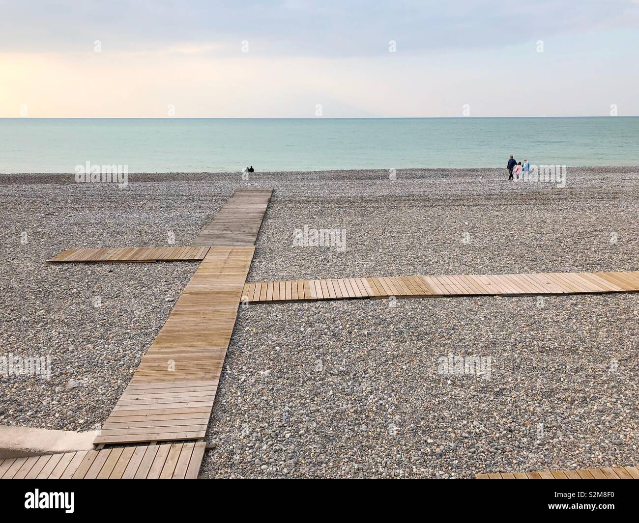 Qualche gente camminare sulla spiaggia di ciottoli di Dieppe in alta stagione con una passerella di legno in primo piano. Foto Stock