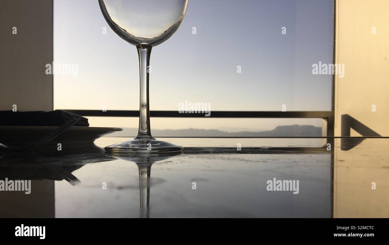 Fondo del bicchiere di vino sul tavolo riflettente nel tardo pomeriggio con montagne in lontananza visibile attraverso la finestra Foto Stock