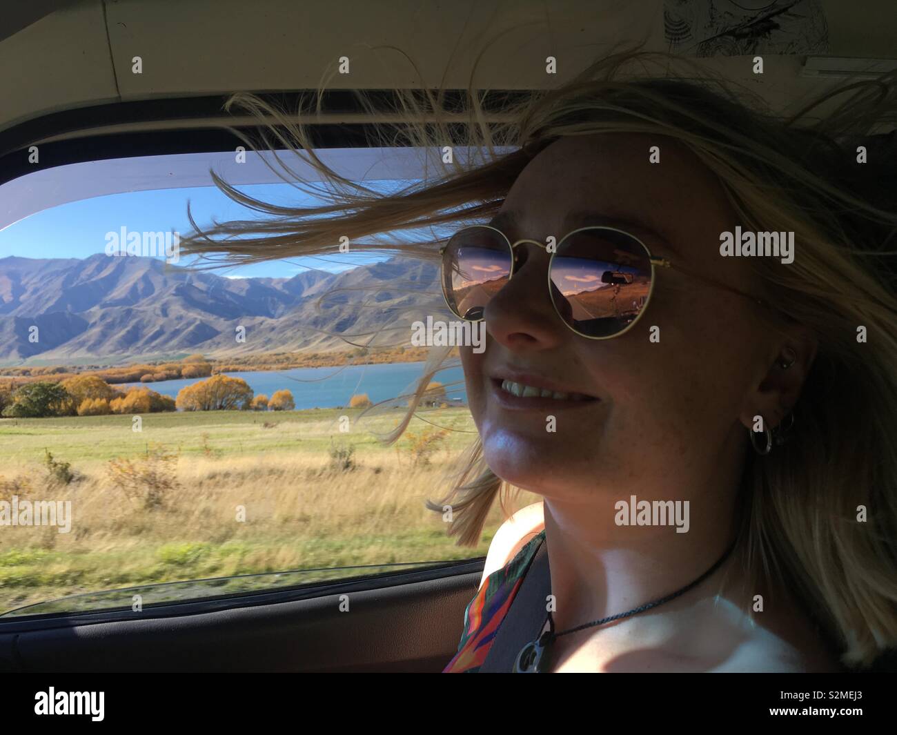 Bella ragazza la guida in campagna con il vento che soffia in aria - Scenic Nuova Zelanda paesaggio in background. Foto Stock