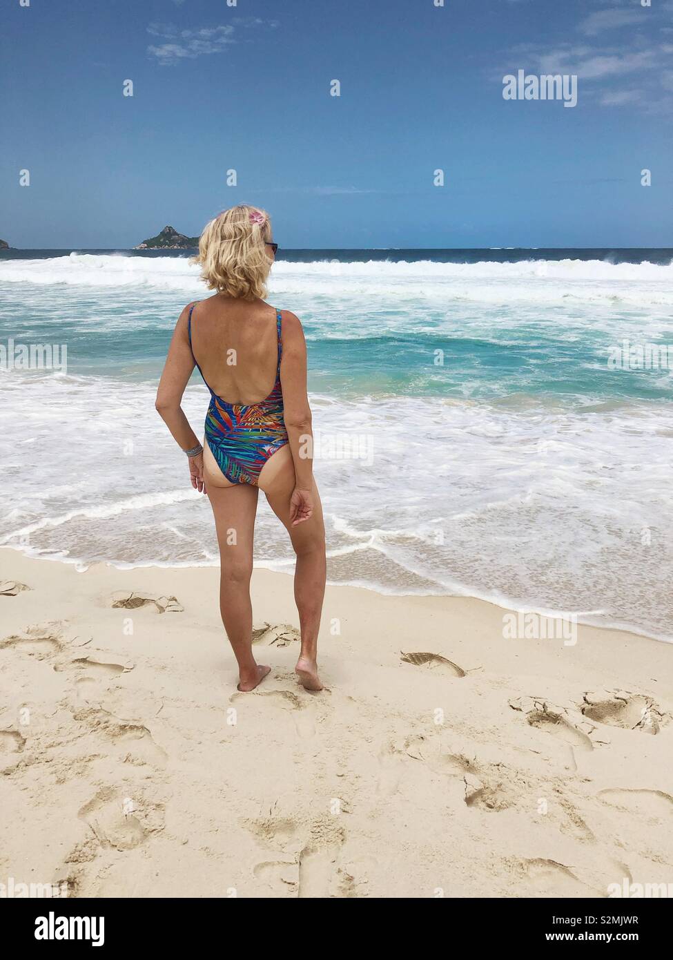 Una donna in piedi sulla spiaggia di fronte al mare. Foto Stock