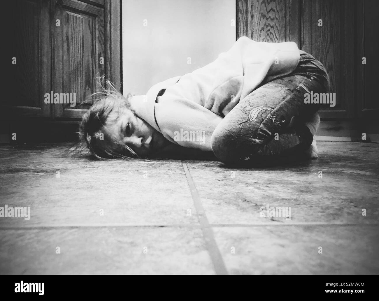 Moody immagine della ragazza giovane rannicchiato sul pavimento della cucina sensazione triste e sconvolto Foto Stock