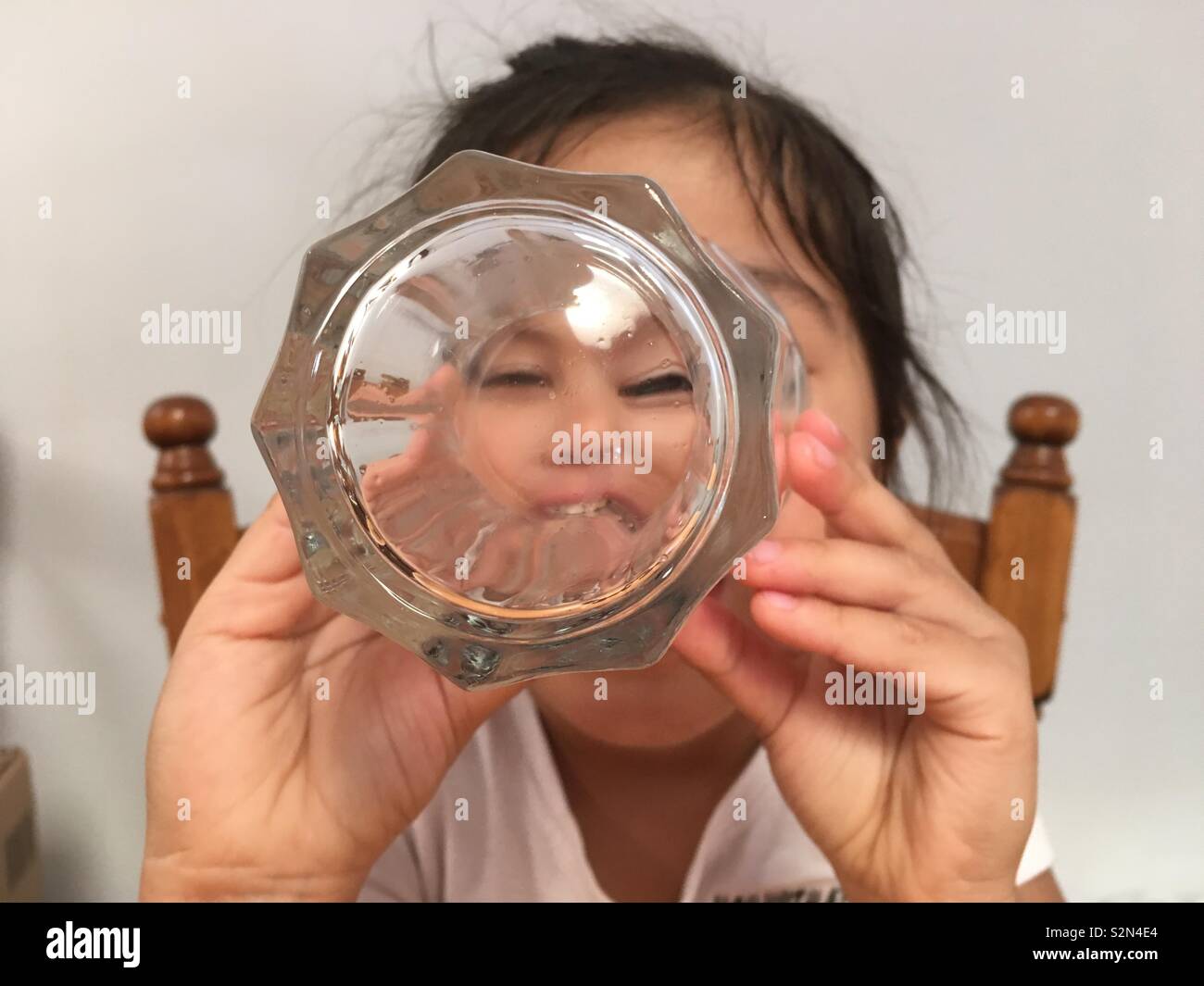 La faccia di un giovane multi-etnico (Caucasica/Punjabi/vietnamita) ragazza cerca attraverso un bicchiere. Foto Stock