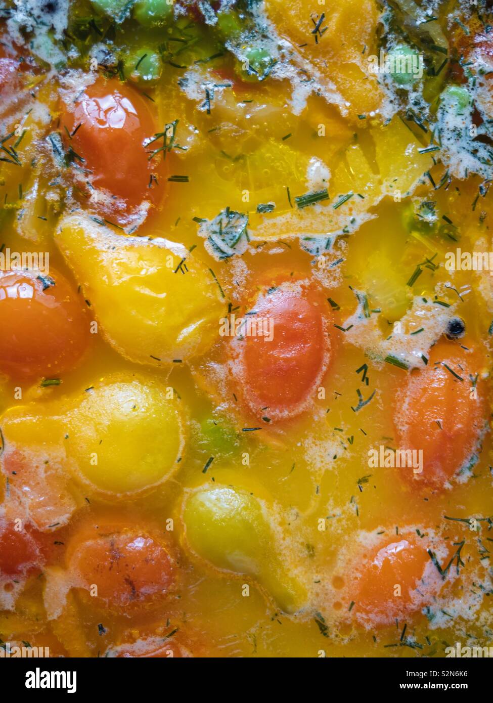 Vista dall'alto sui pomodori ciliegia sprofondando in una zuppa di pesce Foto Stock
