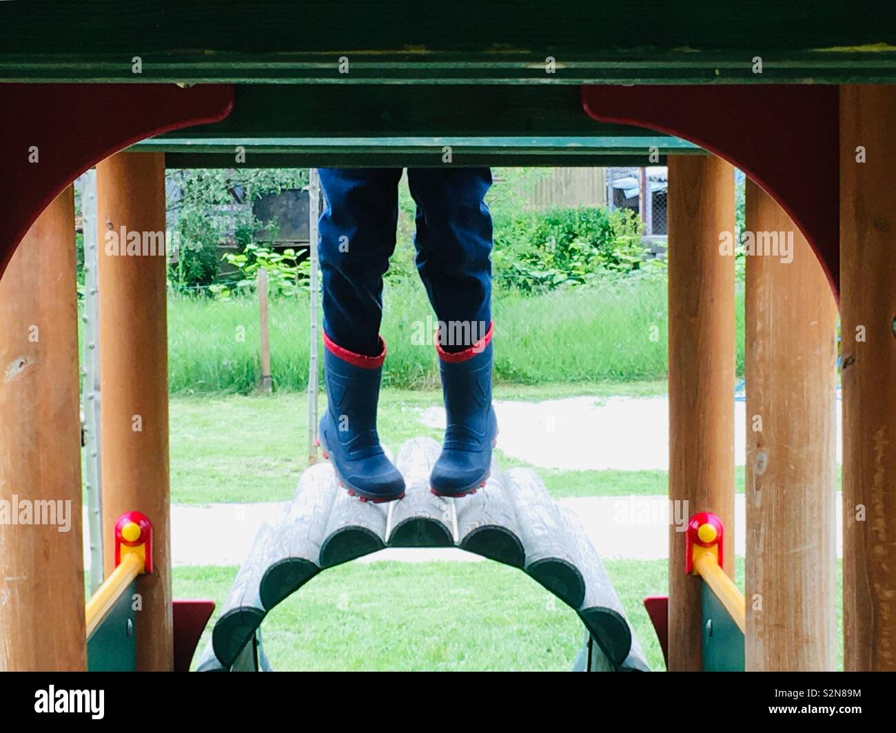 Le gambe del bambino con stivali di gomma appeso durante la salita sul giocattolo di legno treno presso il parco giochi Foto Stock