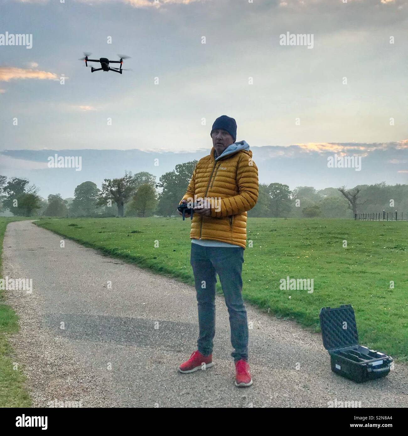 Un drone pilota con drone in volo nella parte anteriore di un prato e giardini nella nebbia - Immagine stock catturata con smartphone