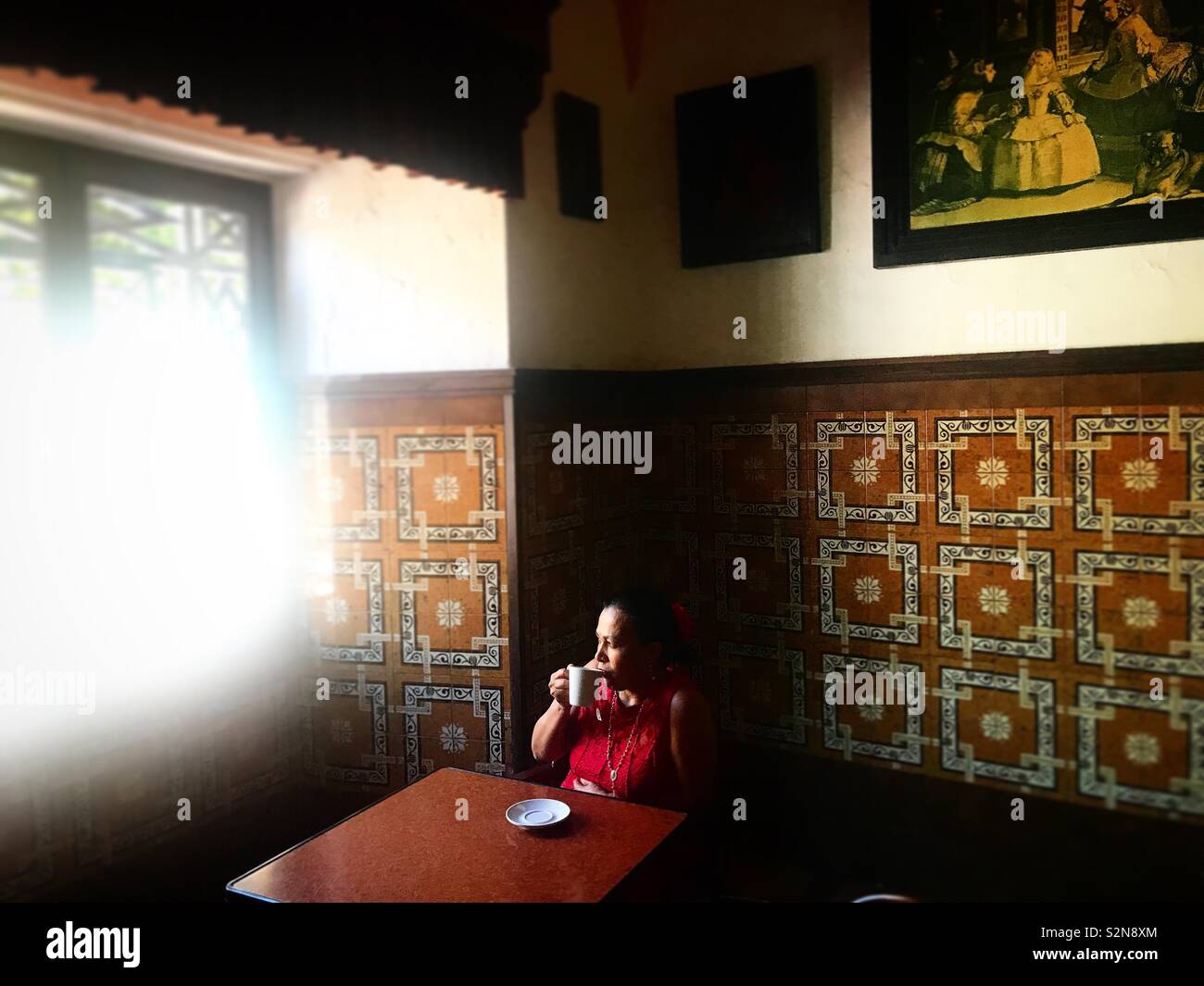 Una donna che beve una tazza di caffè nella caffetteria vicino a una finestra in Prado del Rey, Sierra de Grazalema, Andalusia, Spagna - Immagine stock catturata con smartphone