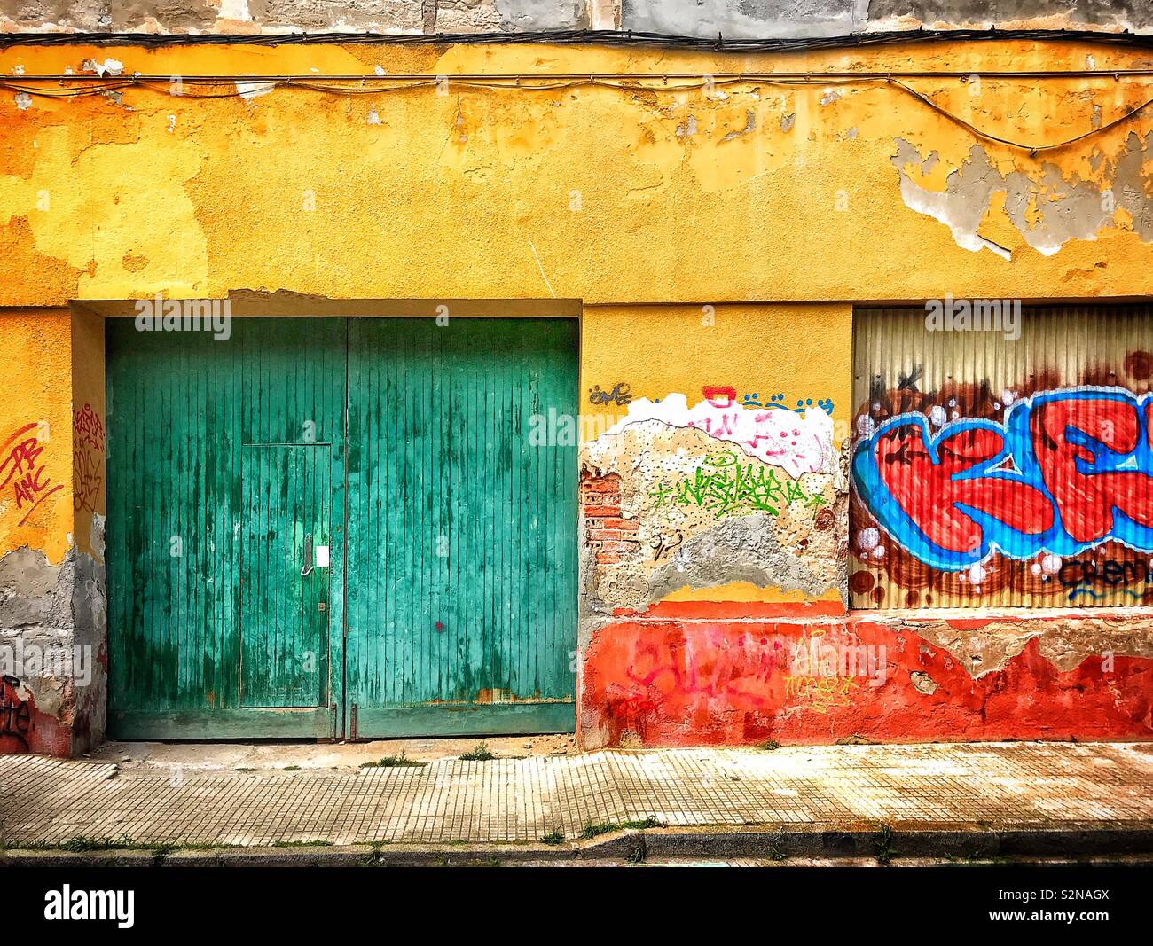 Green le porte di ingresso di un edificio fatiscente spagnolo nel villaggio di pescatori di Santoña, le cui pareti sono intonacato con graffiti. Foto Stock