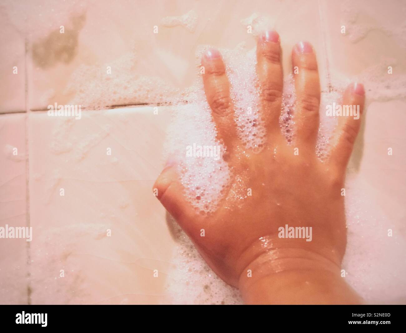 Ragazza giovane d'ulivo e scuoiate mano che poggia contro le piastrelle del bagno. Giocando con le bolle. Foto Stock